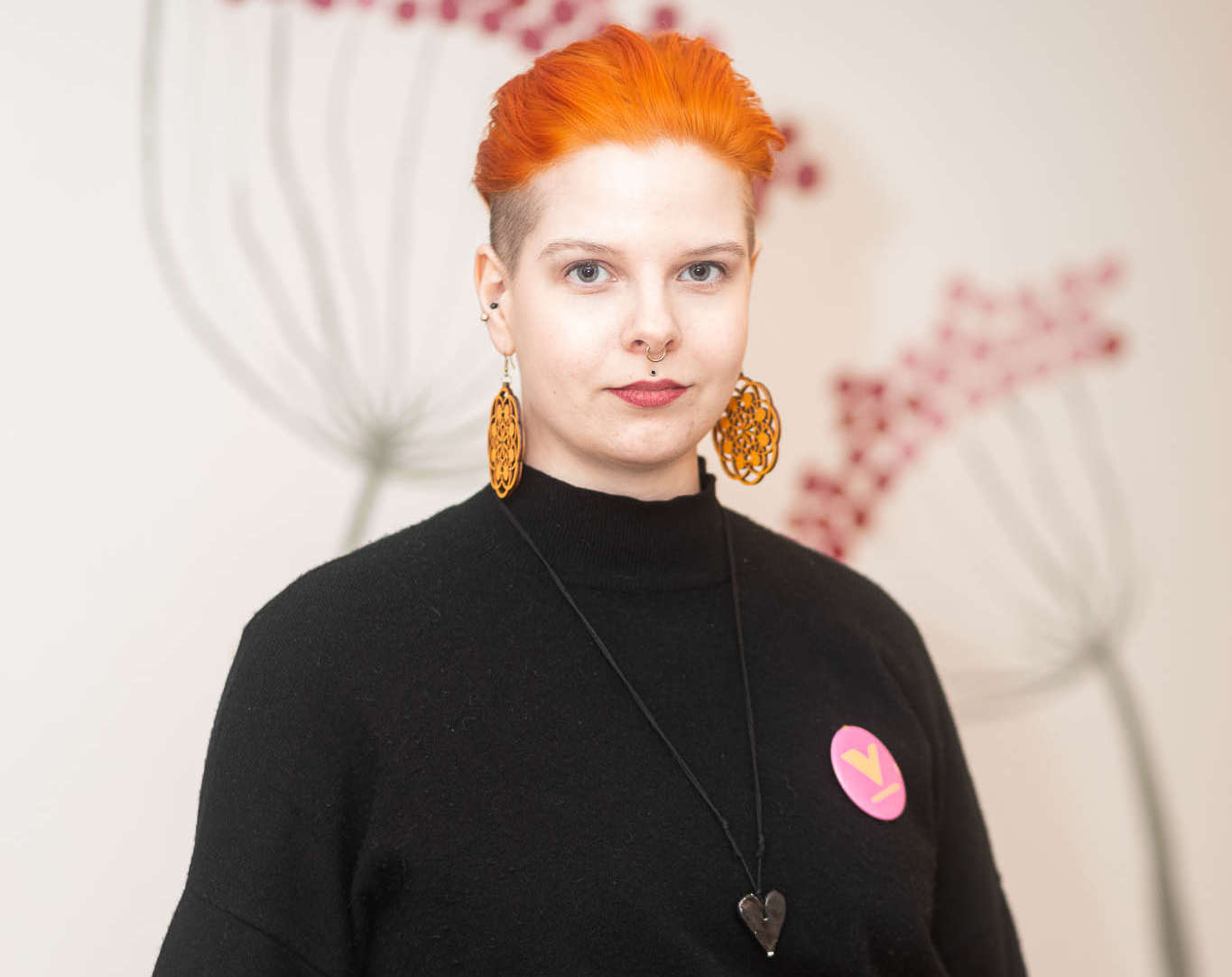 Jenni Jäntti on valkoinen ja hänellä on oranssit lyhyet hiukset. Hän on pukeutunut mustaan ja hänellä on sydänkaulakoru ja suuret korvikset. Rinnassa on vasemmistoliiton rintamerkki.