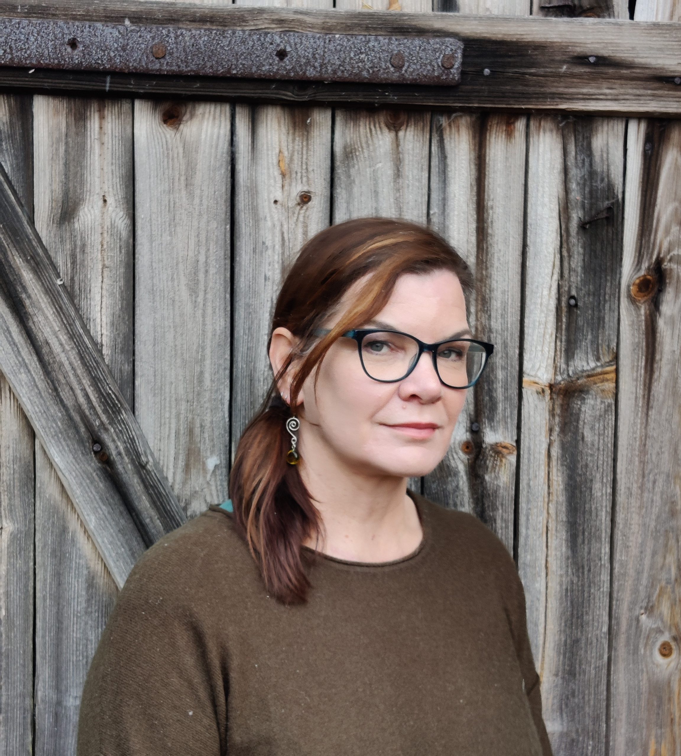 Kaisa Korhonen katsoo kameraan hieman sivuittain, taustalla harmaata ladon seinää.