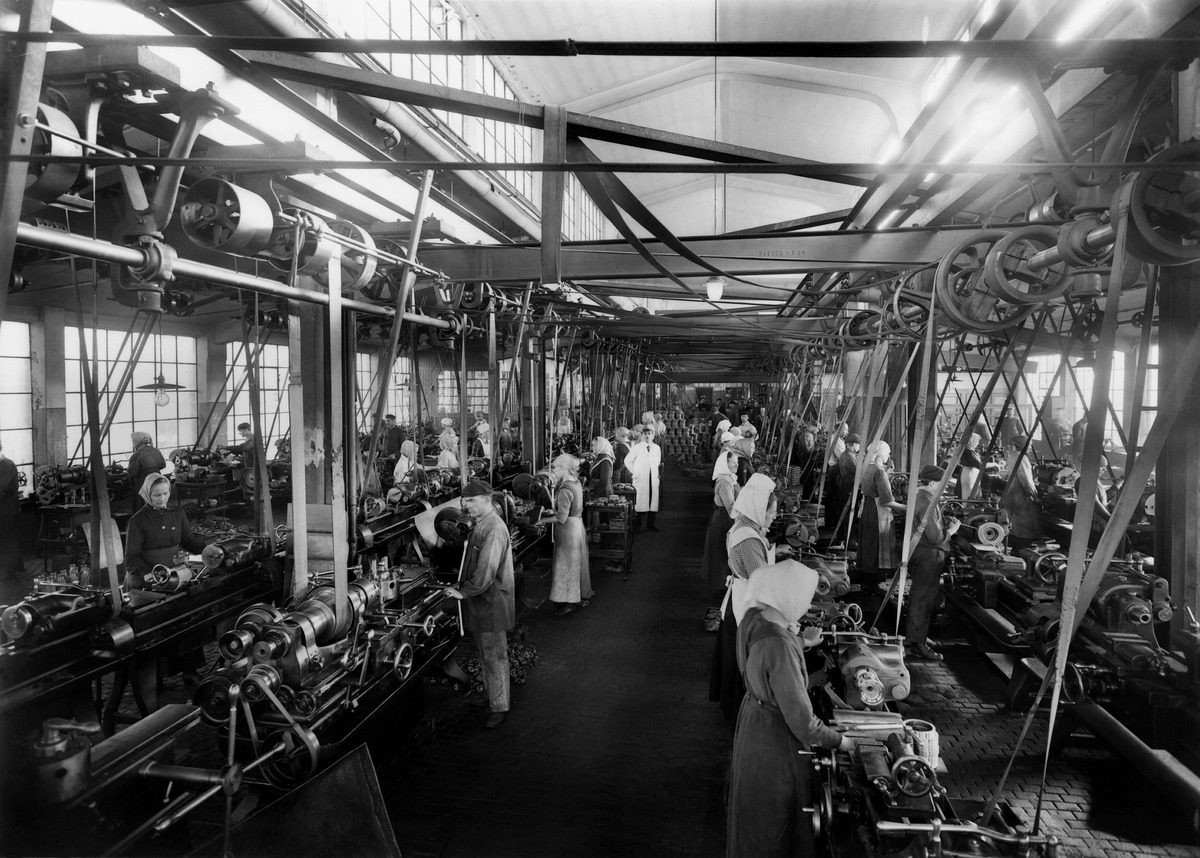 Mustavalkoinen valokuva, jossa työntekijöitä tehtaassa 1910-luvulla.